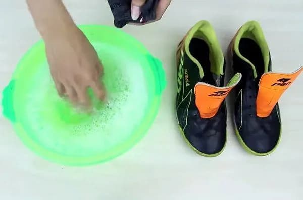 Vệ sinh giày bóng đá bằng dung dịch xà phòng trong chậu nước