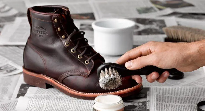 Brushing polish into a leather boot after cleaning, over a layer of newspaper