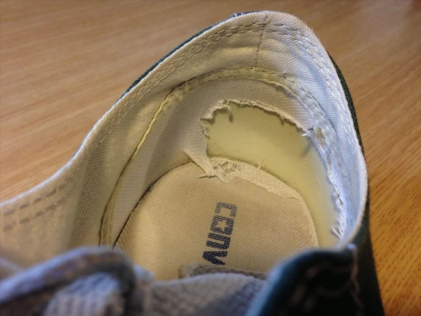 A torn inner lining inside a well-worn canvas shoe