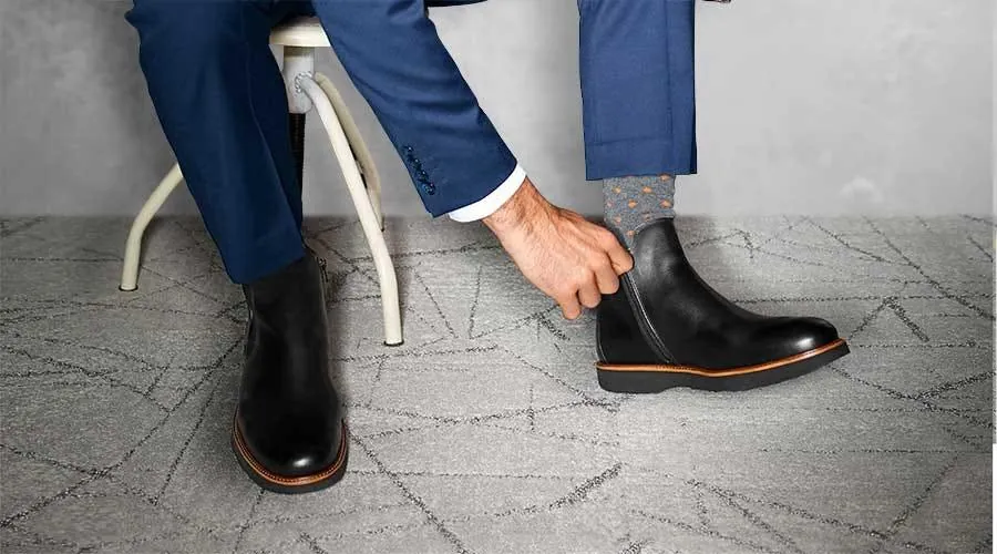 A man pulling on black leather zip boots, the toe area needing its shape kept